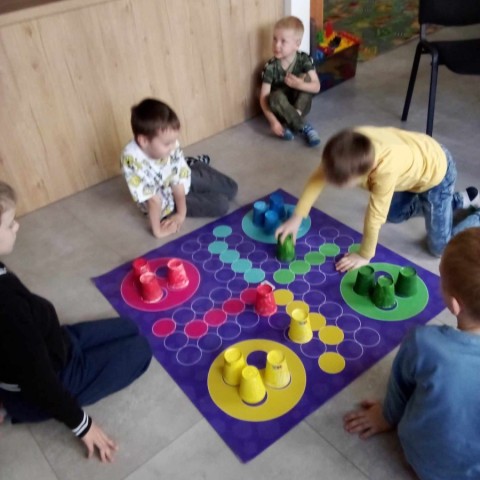 Powiększ obraz: Na zdjęciu dzieci na podłodze grają w grę planszową w rozmiarze XL - gra Chinczyk.